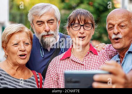 Elderly couples taking selfie with smartphone - Old friends reunion having fun outdoors with each other Stock Photo