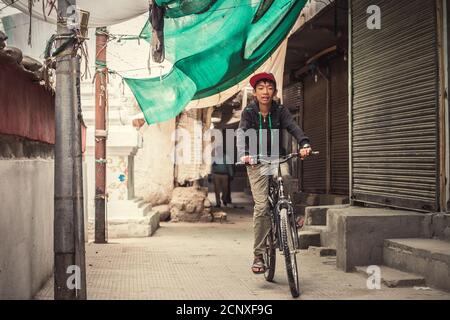 Leh , Ladakh region , India - August 20, 2016: Tibetan teenager boy rides the bike on the Leh narrow street in Leh, India Stock Photo