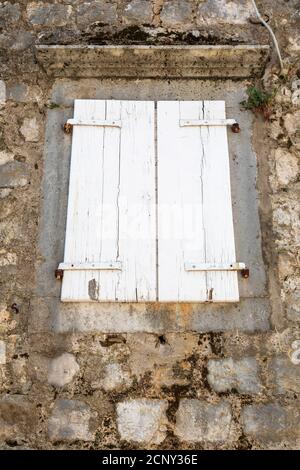 Weathered closed white window shutters on an old abandoned stone seaside house. Stock Photo