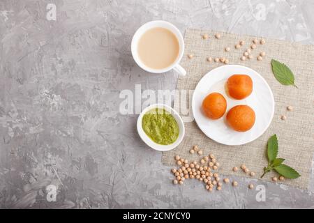 traditional indian candy gulab jamun in white plate with mint chutney on a gray concrete background. top view, copy space, flat lay. Stock Photo