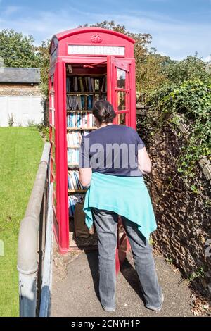 Woman looking at a telephone box in the Norfolk village of West Newton, now used as a villiage library. Stock Photo