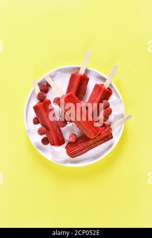 Raspberry ice cream popsicles on white plate over yellow background with free text space. Tasty summer dessert. Top view, flat lay Stock Photo