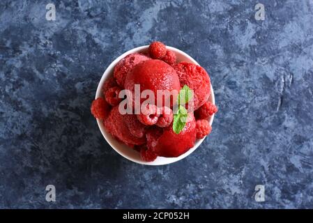 Raspberry sorbet, ice cream scoop with fresh berries in bowl over blue stone background with free text space. Tasty summer cold dessert. Top view, fla Stock Photo
