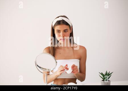 beautiful young woman applying cream on her face at home Stock Photo