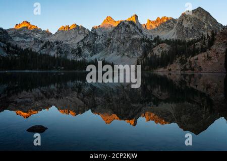 Alice Lake reflects the surrounding peaks at sunrise, Sawtooth Wilderness, Idaho, USA. Stock Photo