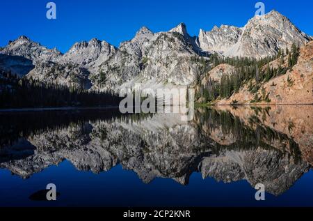 Alice Lake reflects the surrounding peaks under a blue sky, Sawtooth Wilderness, Idaho, USA. Stock Photo
