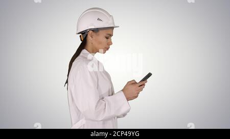 Engineer using mobile phone texting while walking on gradient ba Stock Photo