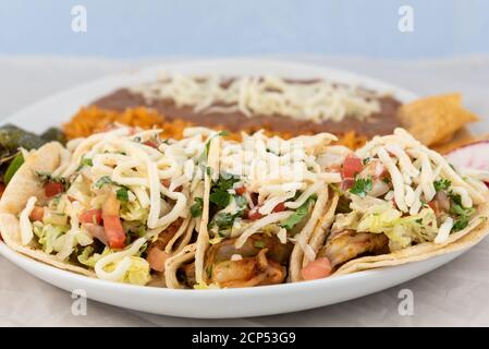 Three shrimp tacos loaded with extras with  rice and beans served on a hot plate for some delicious Mexican food. Stock Photo
