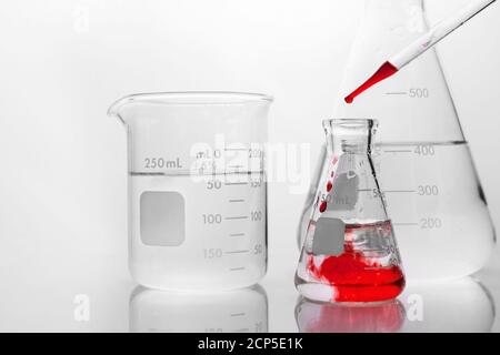 red drop of chemical solution in glass flask in white research science laboratory background