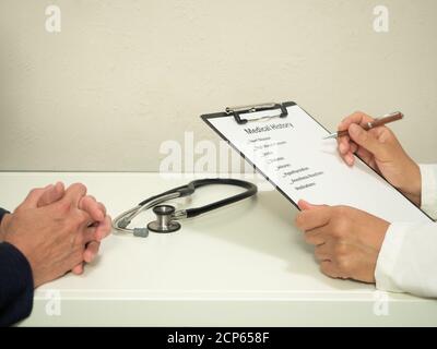 Latina physician's hands with white coat completing medical form with patient's folded hands in photo. Stock Photo