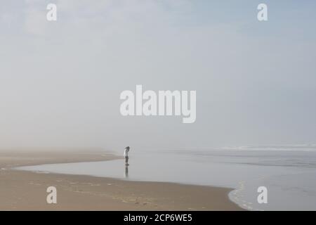 A woman standing alone on a misty beach. Stock Photo