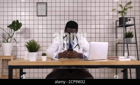 African American Doctor Holding Smart Phone Texting. Stock Photo