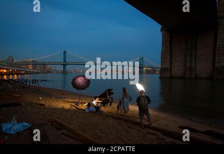 A woman poses for a photo as she leans on a grand piano that has been left beside the East River, during a fashion shoot underneath the Brooklyn Bridge in the Manhattan borough of New York June 3, 2014. According to local media, the piano had been in this space for about a week, puzzling locals as to how it got there and the reason for its placement, perfectly under the bridge.   REUTERS/Carlo Allegri (UNITED STATES - Tags: SOCIETY CITYSCAPE FASHION)