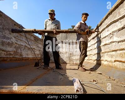 DISTRICT KATNI, INDIA - DECEMBER 09, 2019: Two asian automobile worker installing truck body panel at open area workshop in sky background. Stock Photo