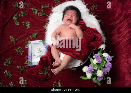 1.5 month baby boy crying while photo shoot rest on while pillow and covering with red velvet shawl Stock Photo