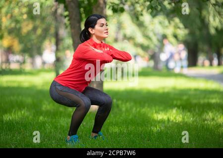 Healthy lifestyle concept. Woman doing exercises for legs in city park. Stock Photo