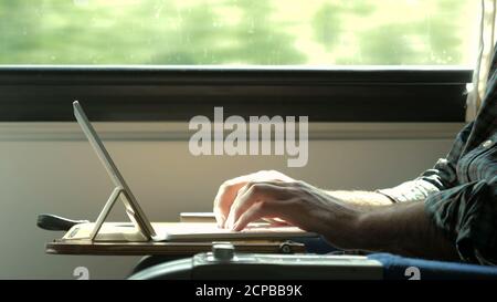 Man hands typing on laptop tablet computer in a train. Stock Photo