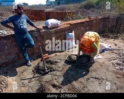 DISTRICT KATNI, INDIA - DECEMBER 13, 2019: An indian female labour picking building material at construction site. Stock Photo