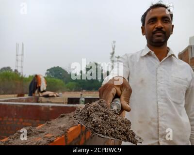 DISTRICT KATNI, INDIA - DECEMBER 18, 2019: An indian village male labour offering cemented building material at home construction site. Stock Photo