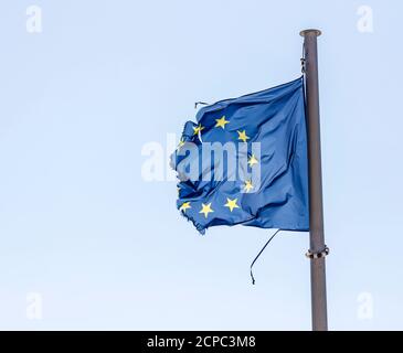 Torn European flag flutters on the flagpole in the wind, symbolic image of EUROPE IN CRISIS.