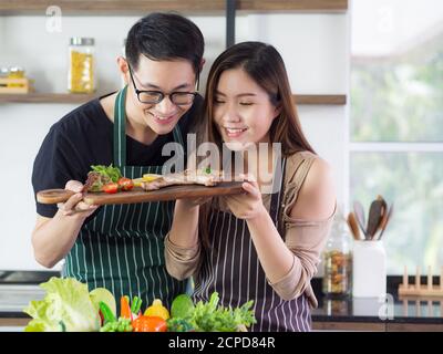 Young couple are very happy after helping to make steak at the kitchen. Concept of couple life Stock Photo