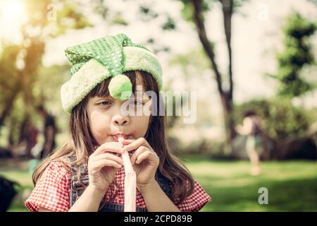 Happy little school girl playing party blow horn on her birthday in the garden in summer. Childhood lifestyles concept. Stock Photo