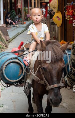A boy rides on a horse in the narrow streets of Ping'an. Stock Photo