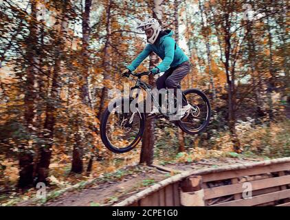 Russia, Moscow - Sep, 2020: Young man jumping with his MTB Bike at forest. Professional downhill riding. Biker riding in nature. Cool athlete cyclist Stock Photo