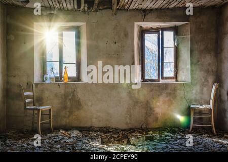 dusty room of an old abandoned house, two straw chairs, two windows and the light that filters through the glass Stock Photo