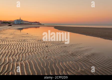 Colorful orange beach at sunset with ripple sand patterns from the receding tide and reflections on the water of the lagoon in a tranquil scenic Stock Photo