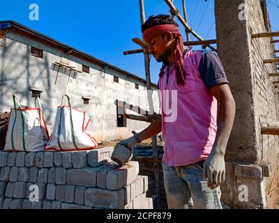 DISTRICT KATNI, INDIA - JANUARY 18, 2020: An indian village male worker constructing cemented brick wall at building construction site in sky backgrou Stock Photo
