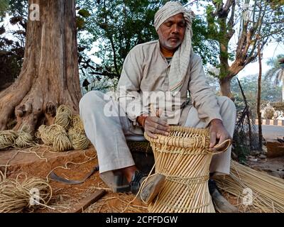 DISTRICT KATNI, INDIA - JANUARY 18, 2020: An indian muslim man making dry grass made chair on open area workshop in natural background. Stock Photo