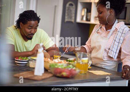 Cheerful Afro-American man and woman having diner in kitchen Stock Photo