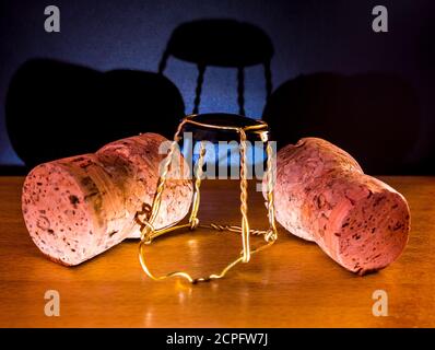 Two cork plugs with muselet(wire cage) from champagne or sparkling wine lies on a wooden surface and cast a shadow on on a dark black-violet Stock Photo