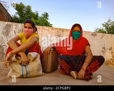 DISTRICT KATNI, INDIA - MAY 21, 2020: Indian village mother and daughter wearing face mask for corona virus protection sitting together with luggage a Stock Photo