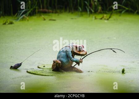 A small frog fishing with a fishing rod ornament in a green lake