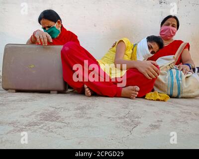 DISTRICT KATNI, INDIA - MAY 21, 2020: Indian village females wearing face mask for corona virus protection sitting together with luggage at sky wall b Stock Photo