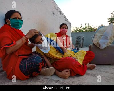 DISTRICT KATNI, INDIA - MAY 21, 2020: Asian village females wearing face mask for corona virus protection sitting together with luggage at sky wall ba Stock Photo