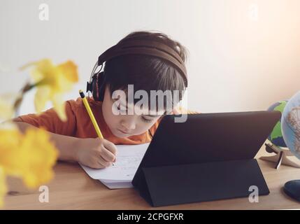 Kid self isolation using tablet for his homework, Child doing  using digital tablet searching information on internet while school of during covid-19 Stock Photo