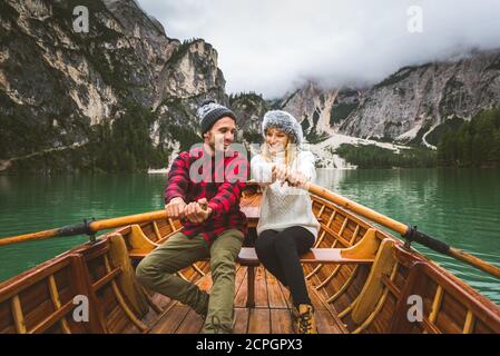 Beautiful couple of young adults visiting an alpine lake at Braies, Italy - Tourists with hiking outfit having fun on vacation during autumn foliage - Stock Photo