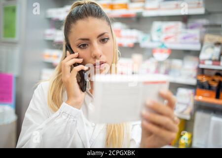 Pharmacist checking drug in a pharmacy while talking on the phone Stock Photo