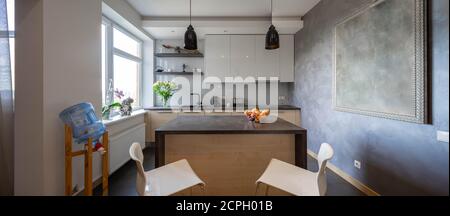 Contemporary interior of kitchen in luxury flat. Wooden kitchen set with dark counter. Fruits on table. Stock Photo