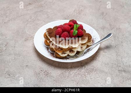 portion of Classic tiramisu dessert with raspberries on grey concrete background Stock Photo