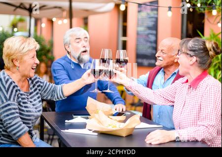 Happy senior friends smiling  and toasting red wine at bar - Elderly people eating at restaurant - Drinking lifestyle concept - Focus on blond lady Stock Photo
