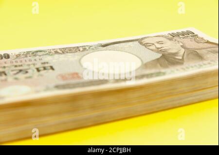 Ten thousand yen (10,000 yen) banknotes stacked. Japanese money. Paper money. Isolated on yellow background. Side view. Close-up. Stock Photo