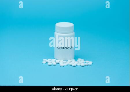 AZITROMYCIN antibiotic in white bottle packaging with scattered pills. Treatments for COVID-19. isolated on blue background. Copy space. Stock Photo