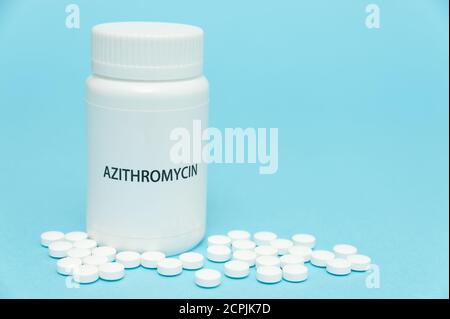 AZITROMYCIN antibiotic in white bottle packaging with scattered pills. Treatments for COVID-19. isolated on blue background. Copy space. Close-up. Stock Photo