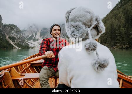 Beautiful couple of young adults visiting an alpine lake at Braies, Italy - Tourists with hiking outfit having fun on vacation during autumn foliage - Stock Photo