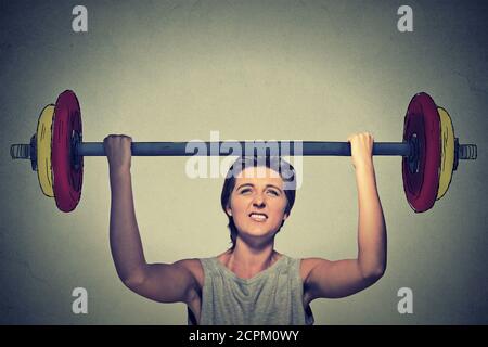 Strong woman lifting heavy barbell isolated on gray wall background. Determination task completion hard work concept Stock Photo