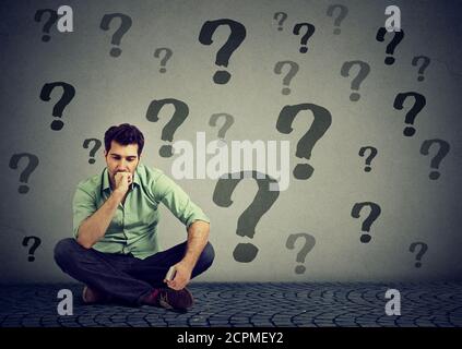 young business man sitting on a floor in front of wall with many questions wondering what to do next. Businessman facing life challenge. Job work prob Stock Photo
